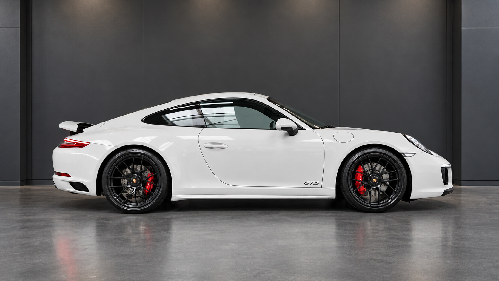 Vit Porsche 911 i profil i ett mörkt showroom, med hela bilen synlig